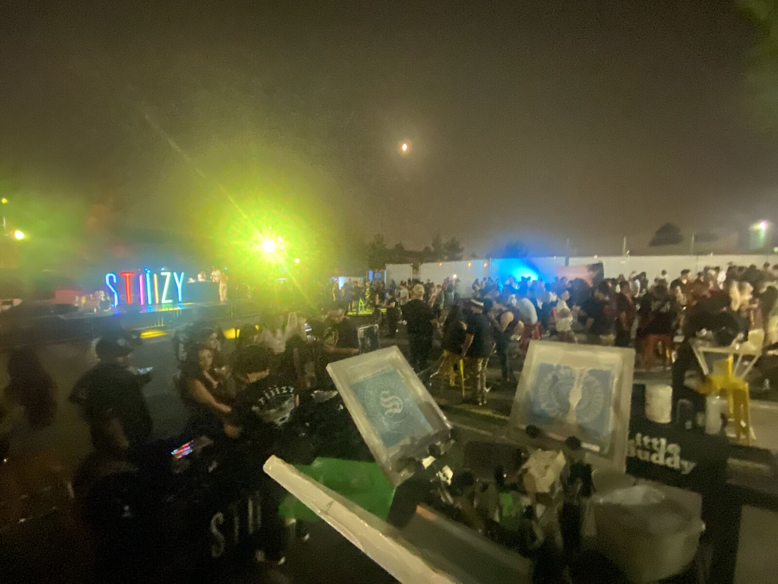 Nighttime festival venue with purple ambient lighting and crowds of attendees