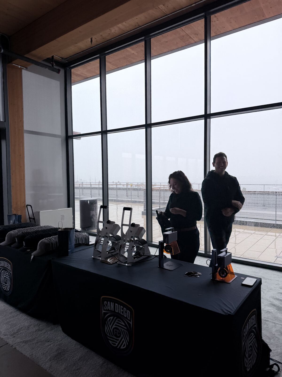 Booth operators at a street-level live printing event with urban architecture visible through the window