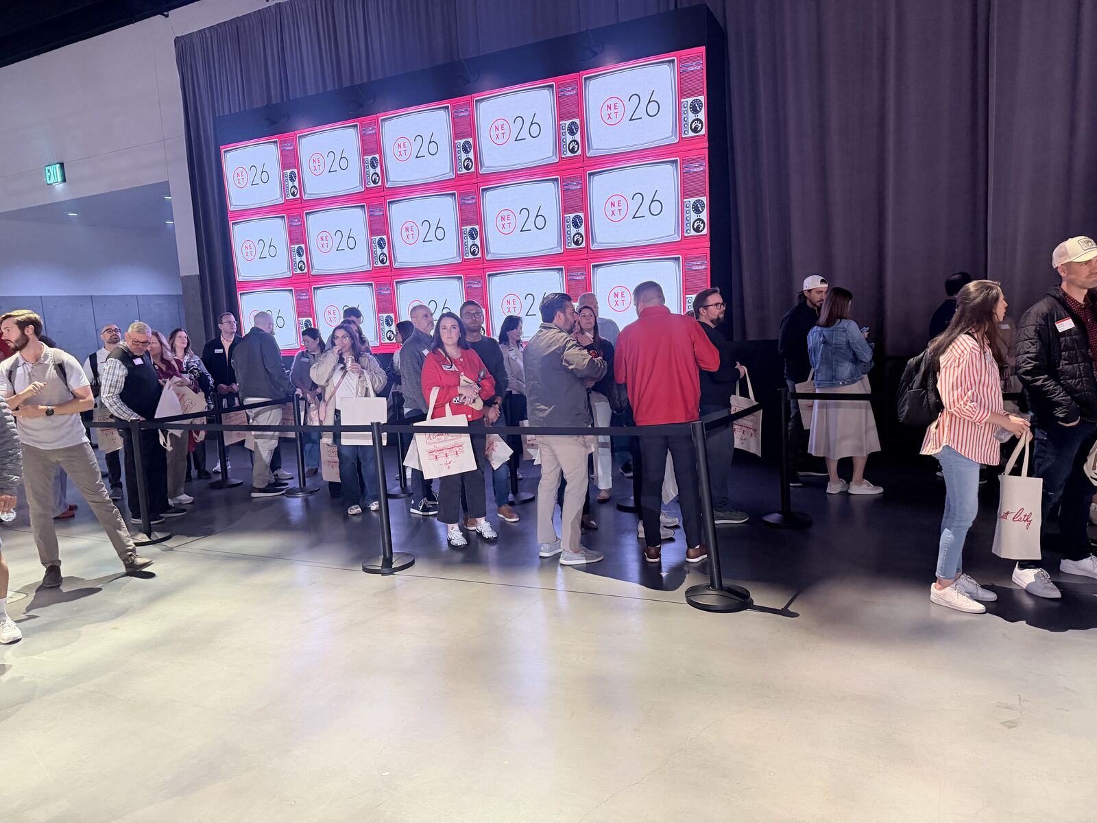 Festival crowd lined up in front of a large pink neon display wall holding branded totes