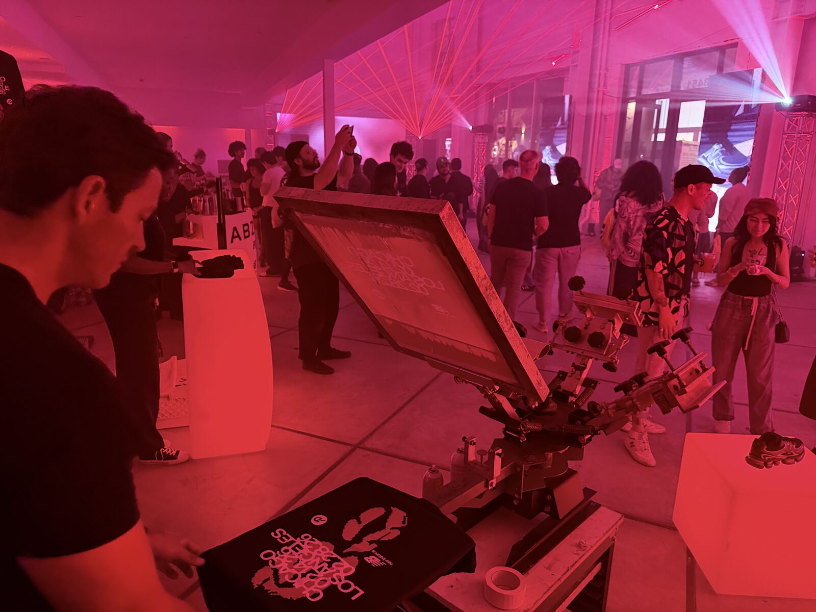 Packed event space bathed in magenta neon lighting with dozens of attendees mingling under dramatic ceiling installations